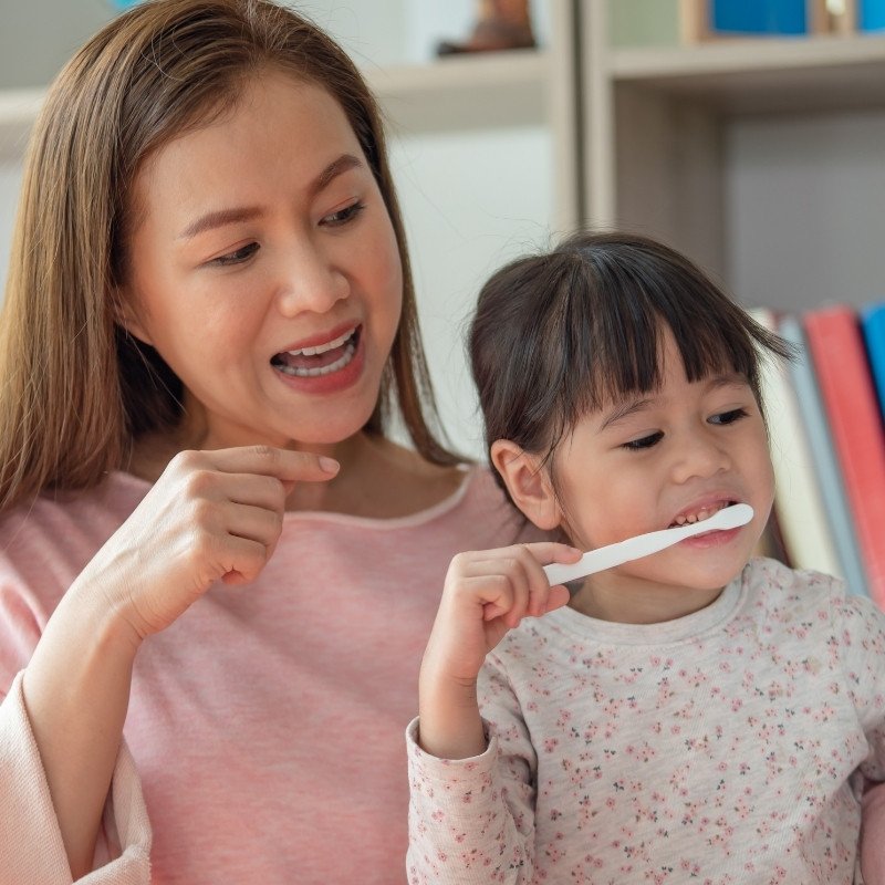 Mother showing child how to brush their teeth